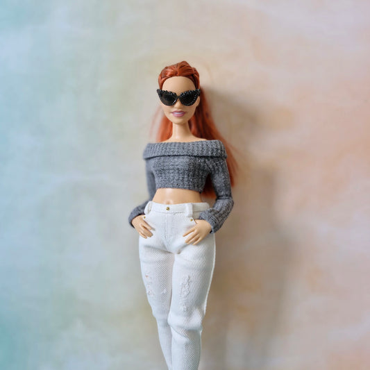 Barbie doll wearing a gray off-shoulder top and white pants with a blurred background