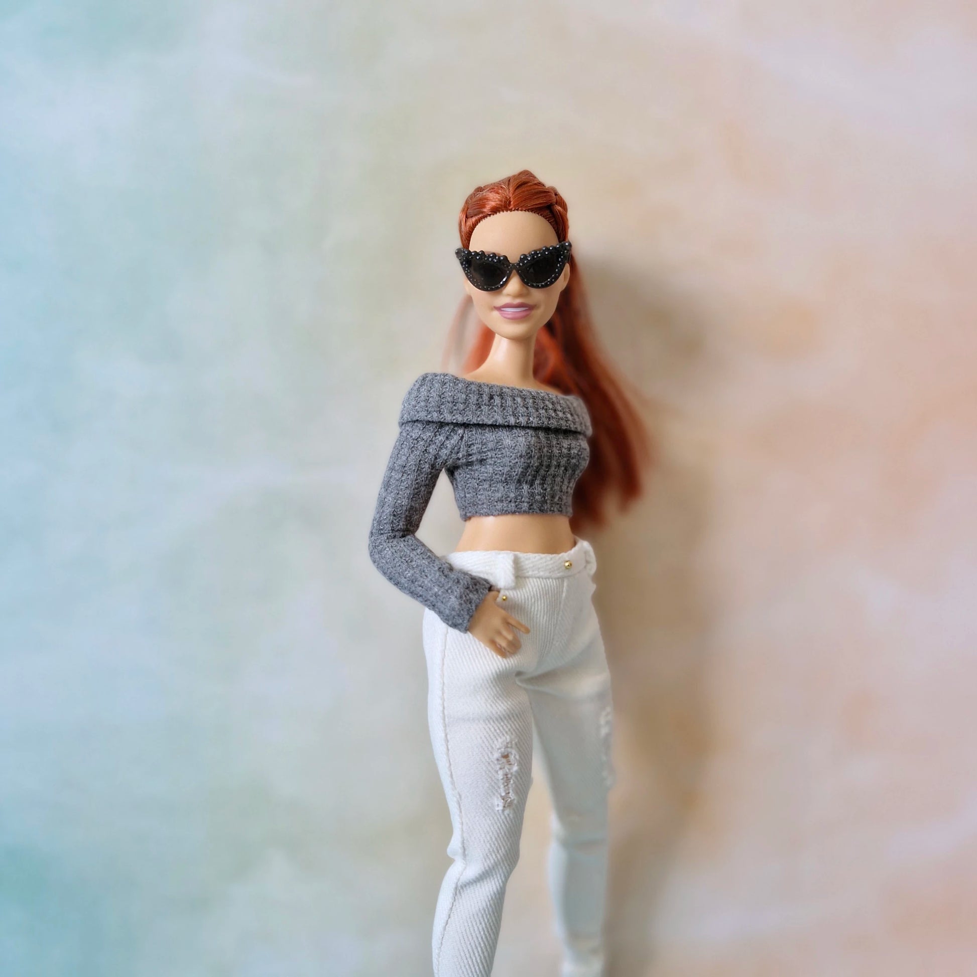 Barbie doll wearing a gray sweater and white pants with a blurred background