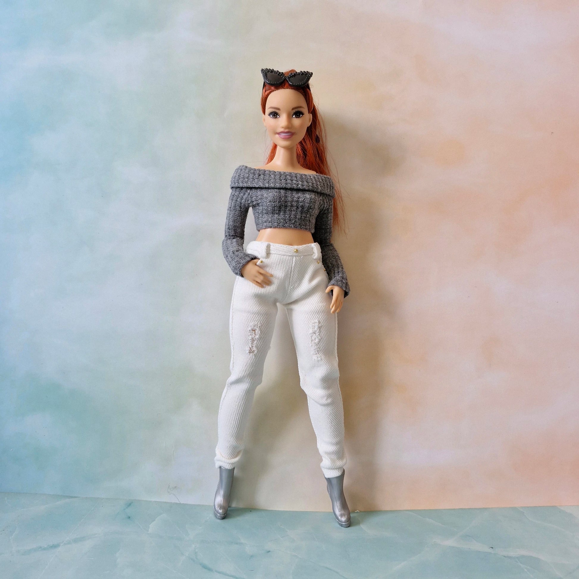Barbie doll wearing a gray off-shoulder top and white pants against a gradient background