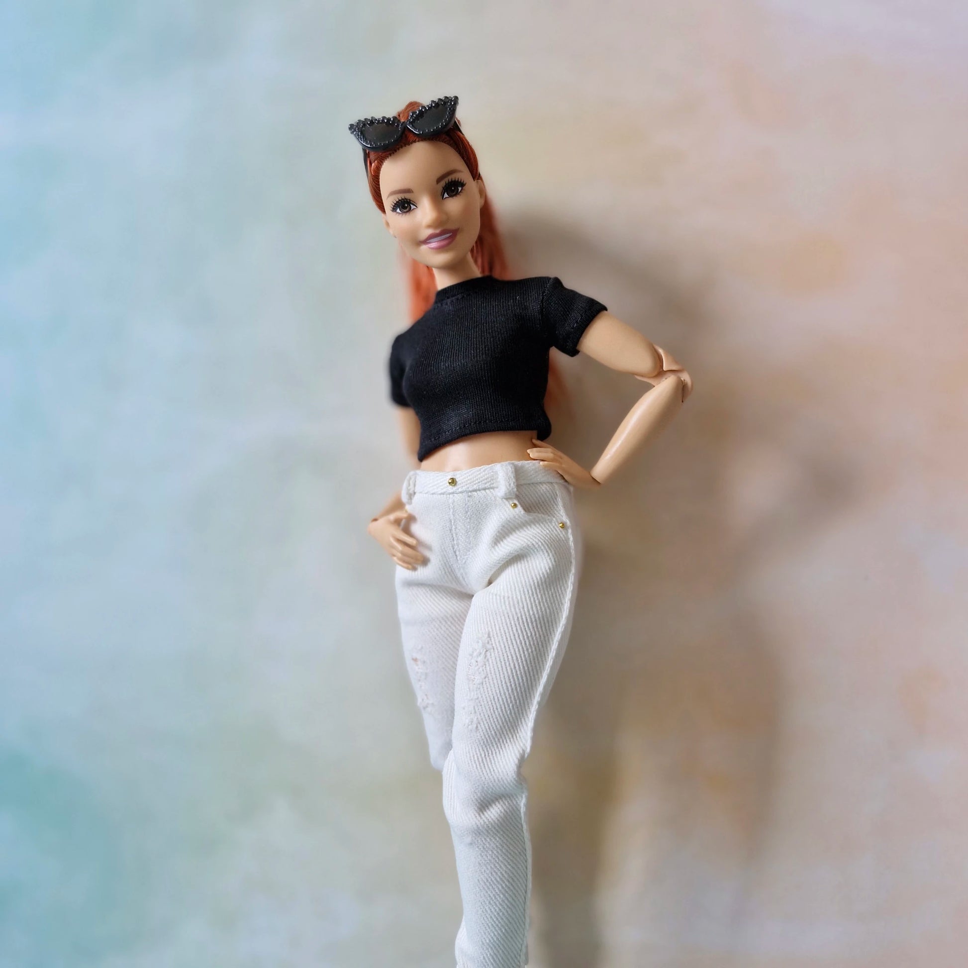 Barbie doll with black top and white pants against a gradient background
