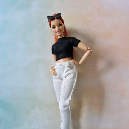 Barbie doll with black top and white pants against a gradient background