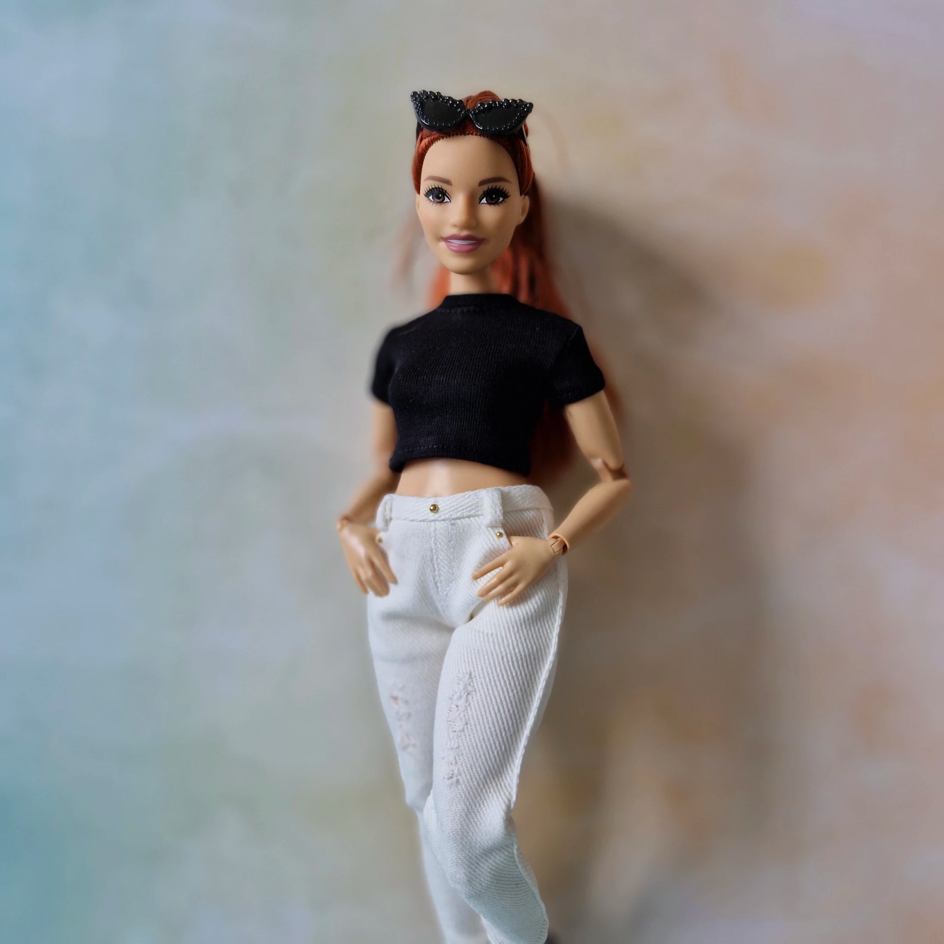 Barbie doll wearing a black top and white pants against a neutral background