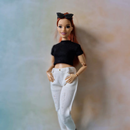 Barbie doll wearing a black top and white pants against a neutral background