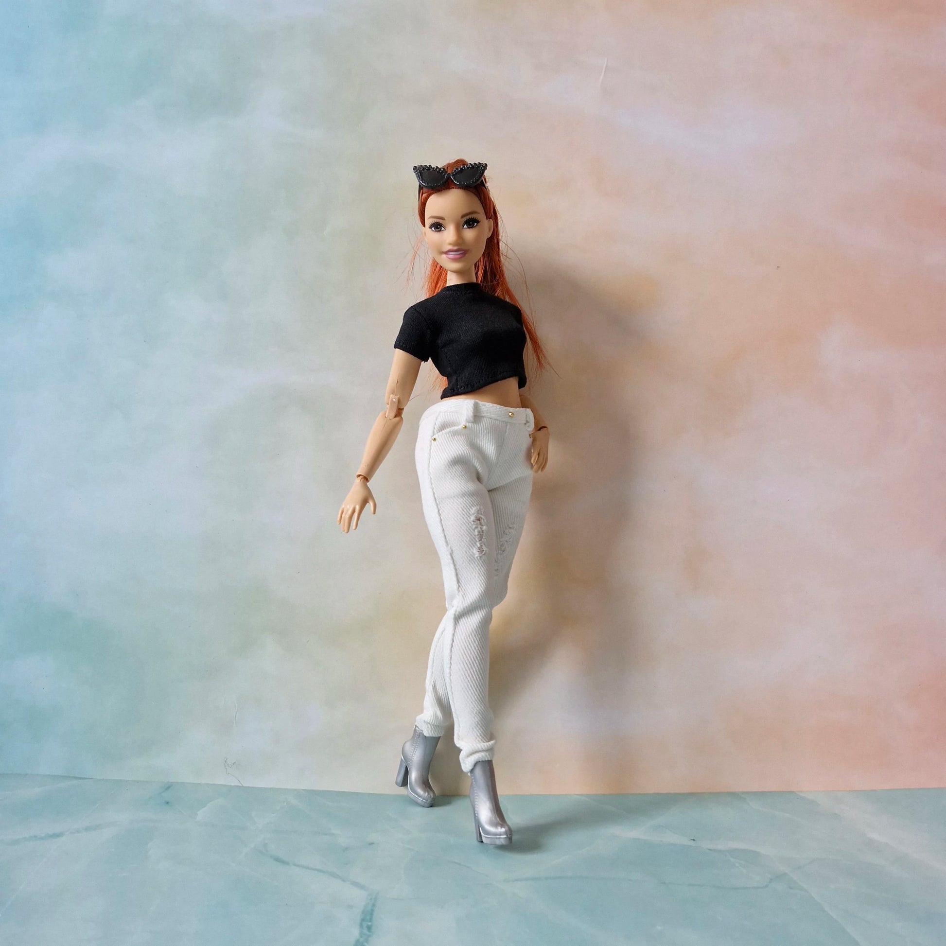 Barbie doll with red hair and black top against a gradient background