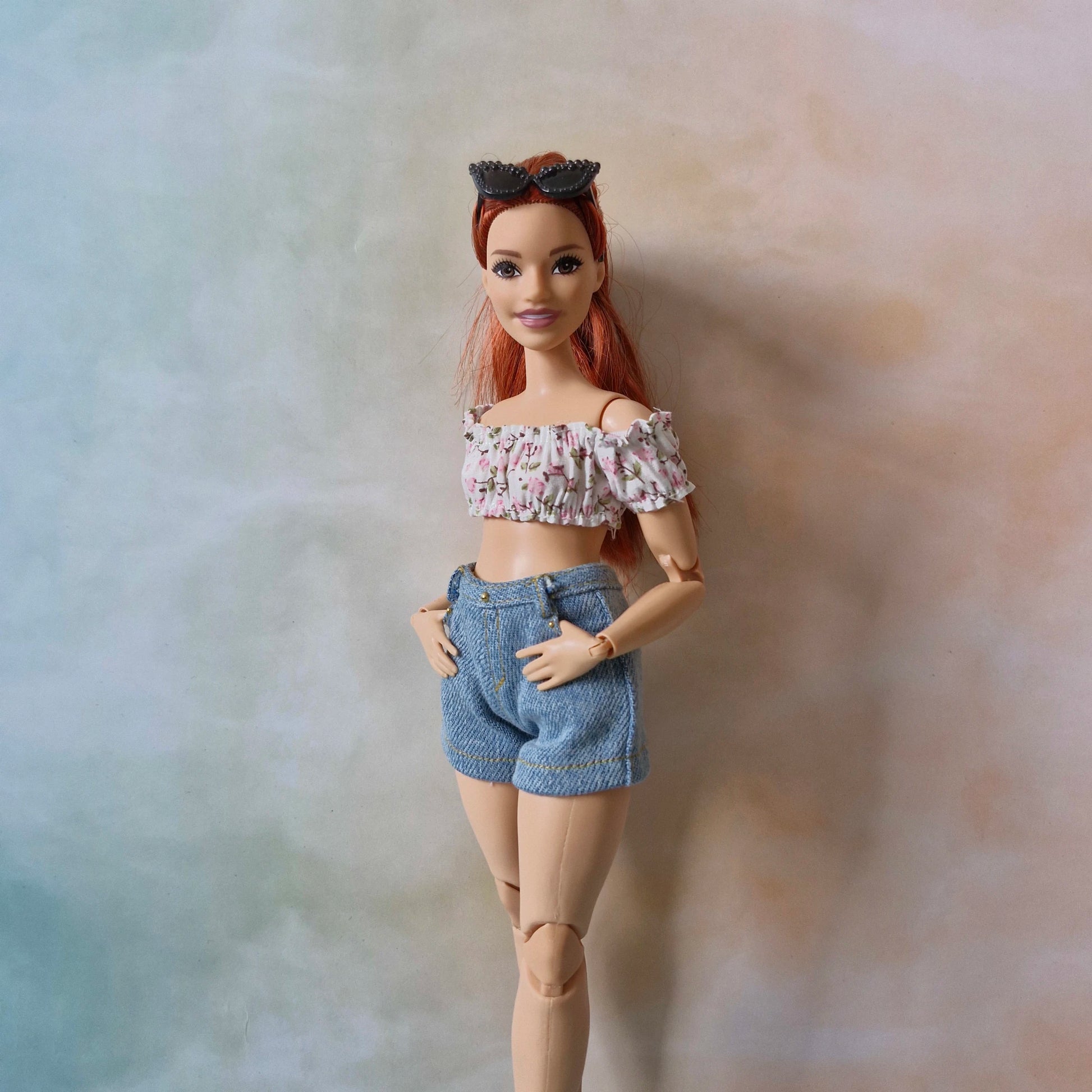 Curvy Barbie doll in a summer outfit with a pink floral top and jean shorts.
