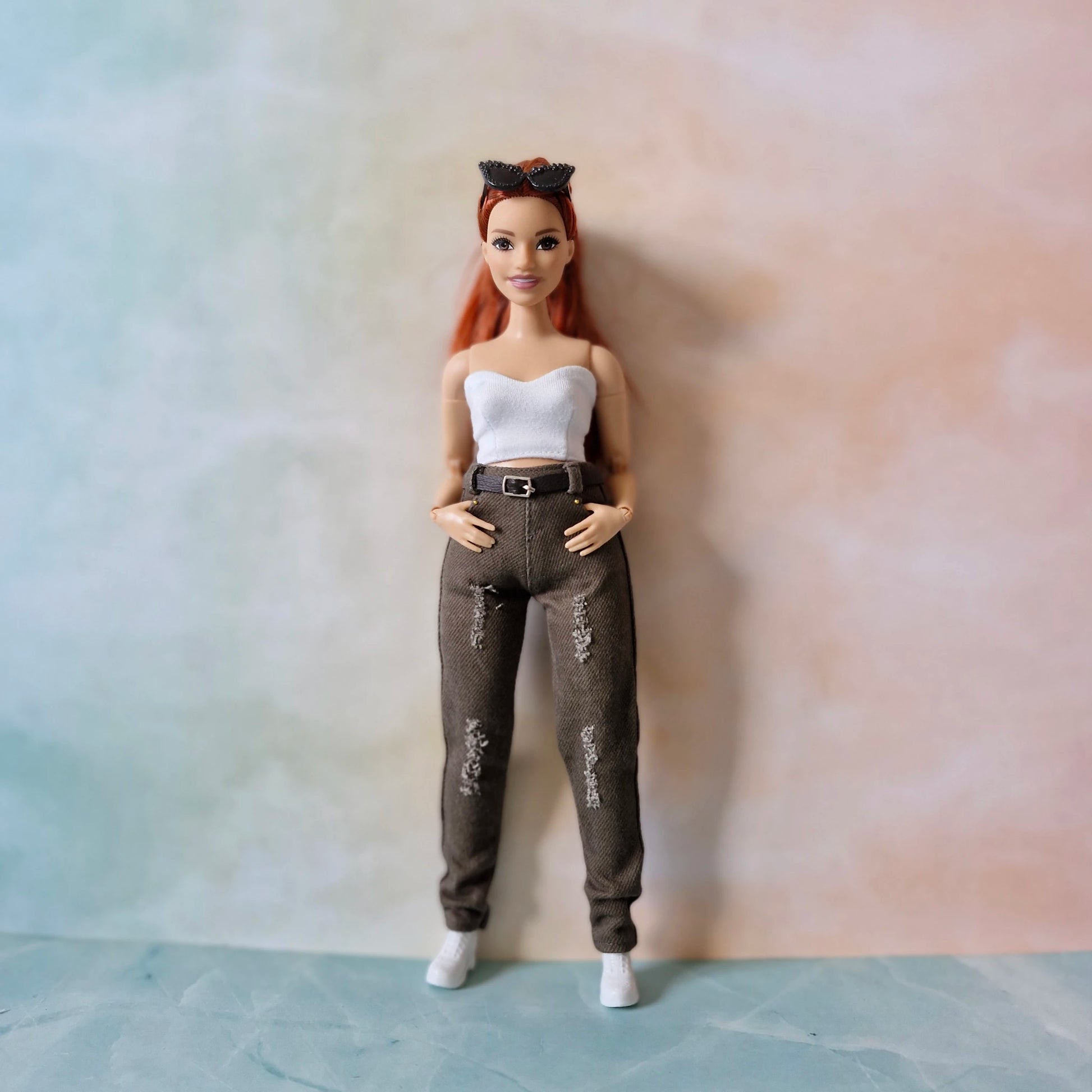 Curvy  Barbie doll with red hair wearing a white top and gray pants against a plain background