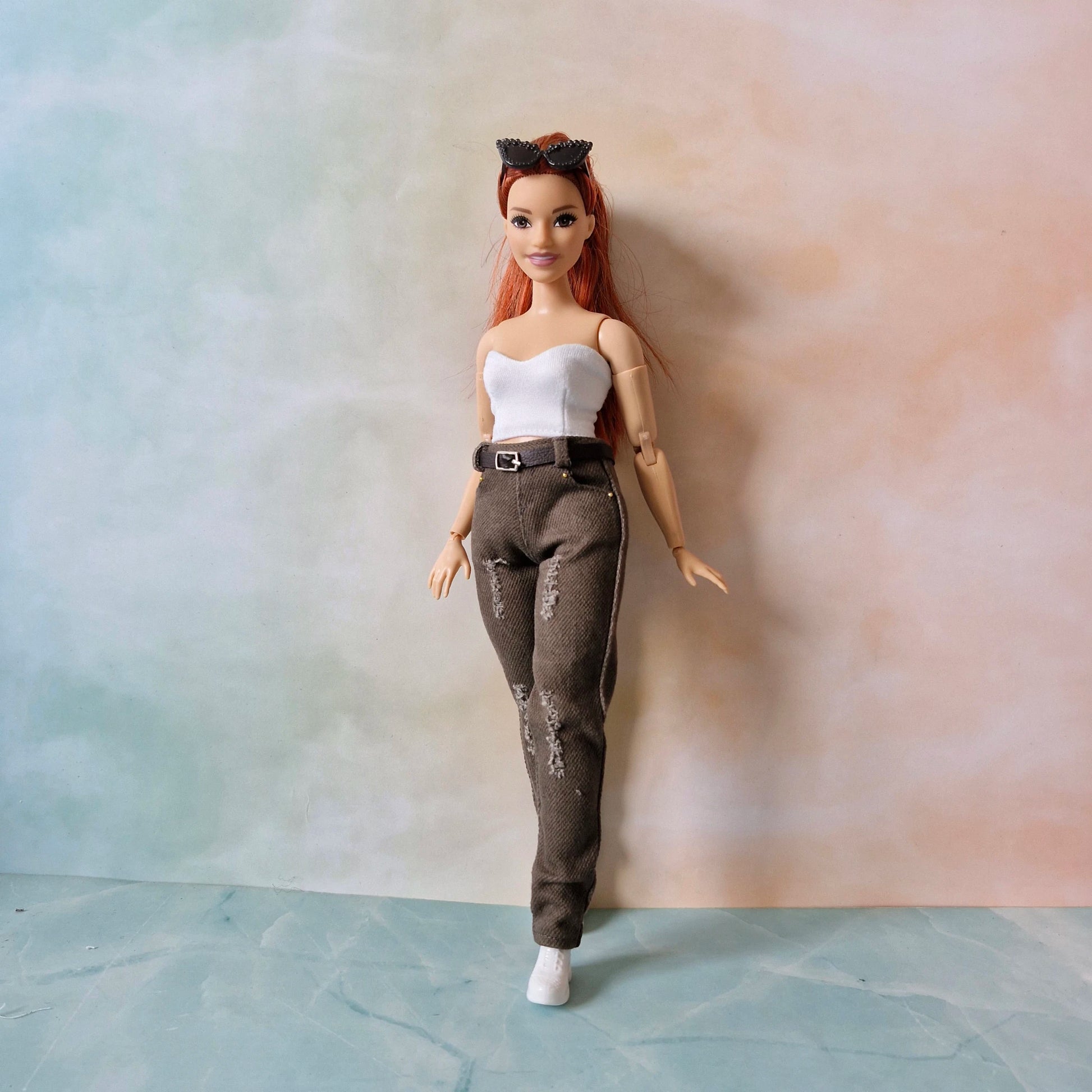 Curvy  Barbie doll with red hair and a white top standing against a gradient wall.