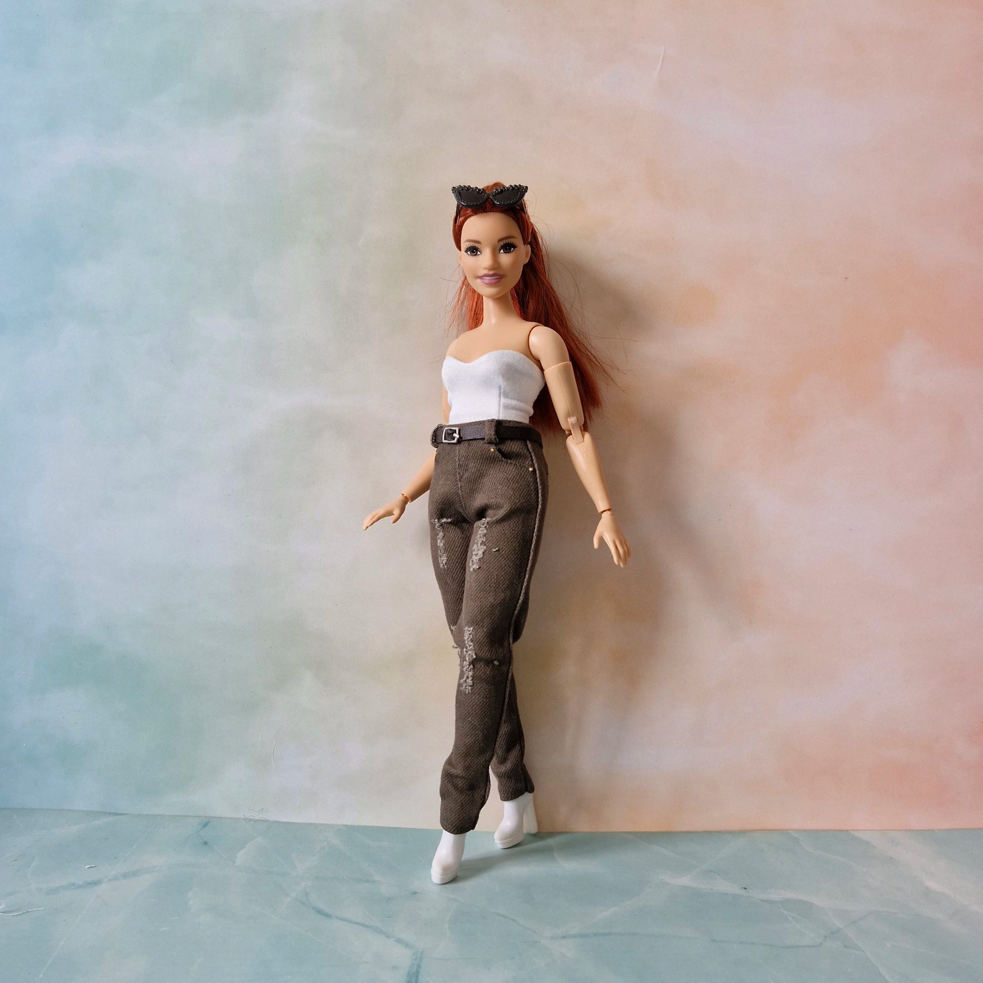 Curvy Barbie doll with red hair and a white top and brown pants against a gradient background