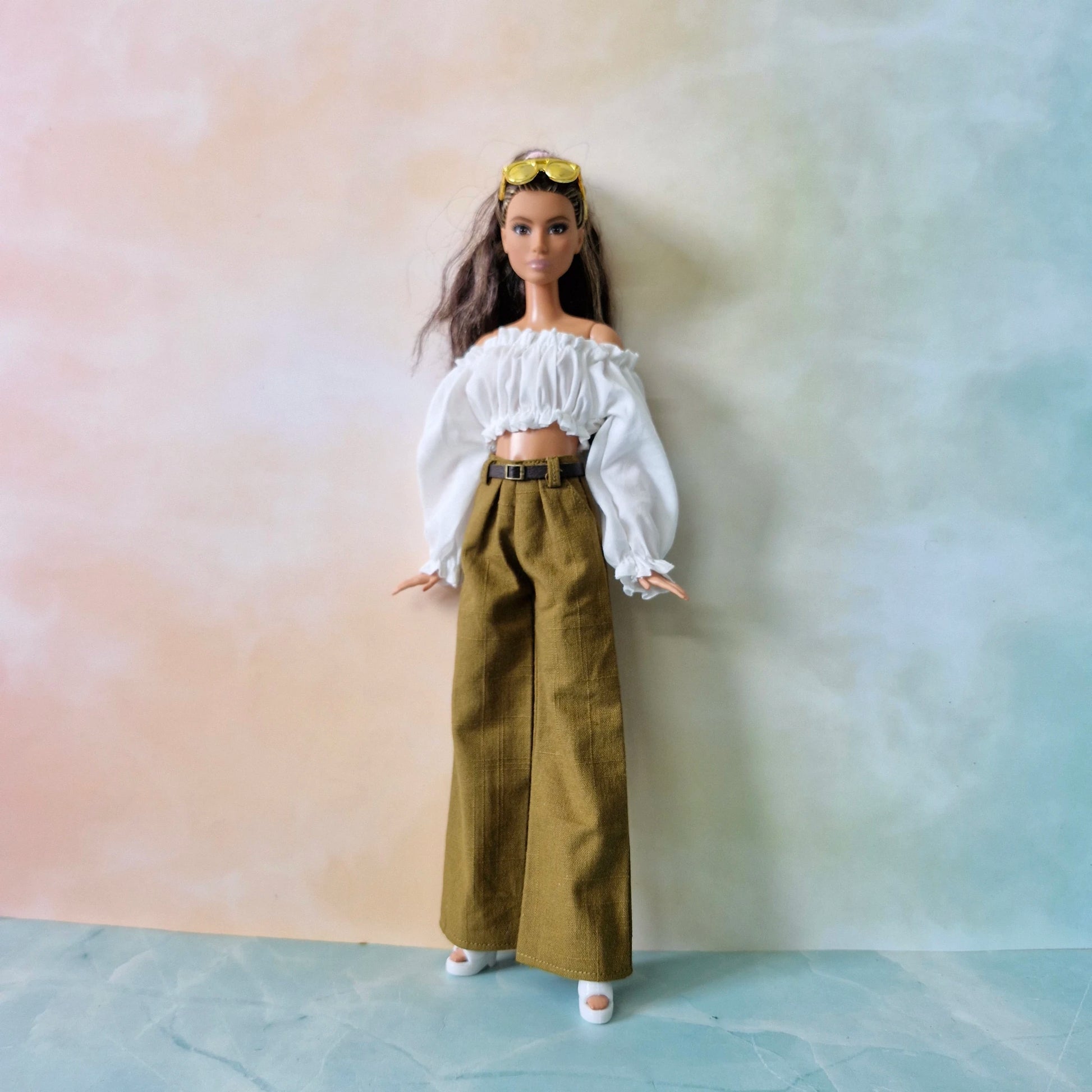 Barbie doll wearing a white top and brown pants against a gradient background