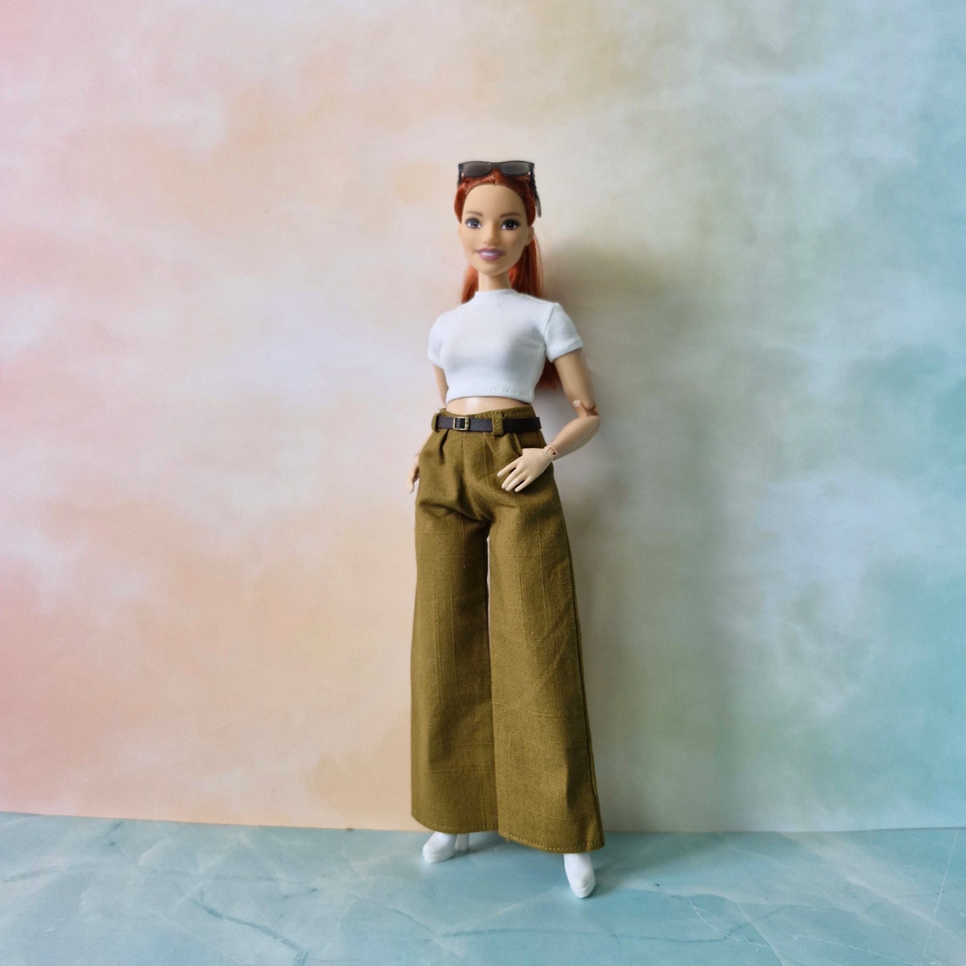 Barbie doll with red hair wearing a white top and brown pants against a gradient background