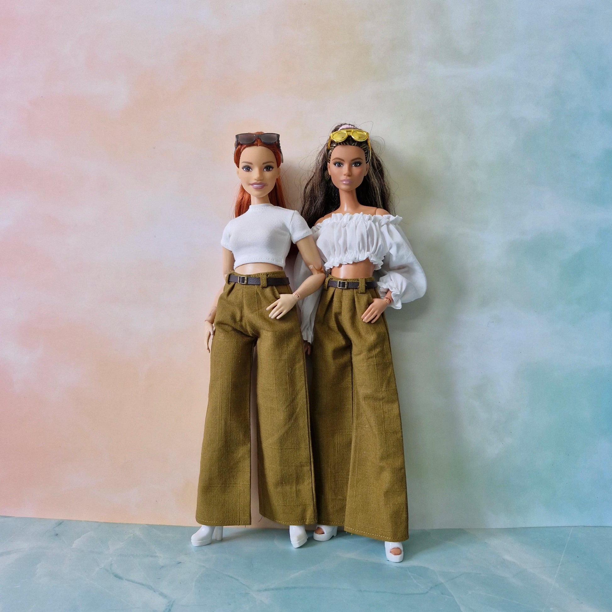 Two dolls wearing matching outfits with wide-leg pants against a pastel gradient background