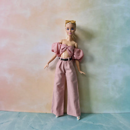 Barbie doll wearing a pink outfit with a bow top and wide-leg pants against a gradient background.