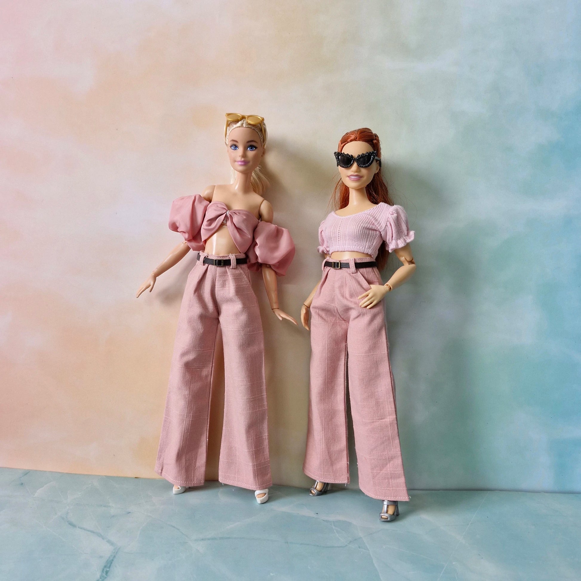 Two dolls wearing matching outfits against a gradient background