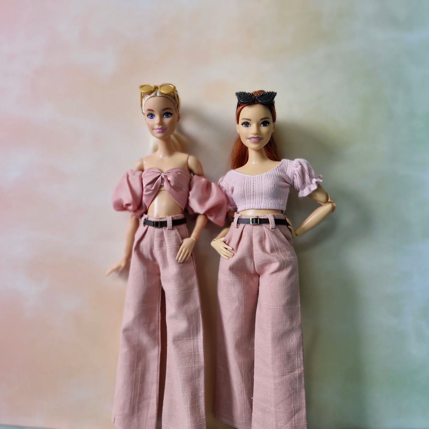 Two dolls wearing matching outfits with a soft pink background