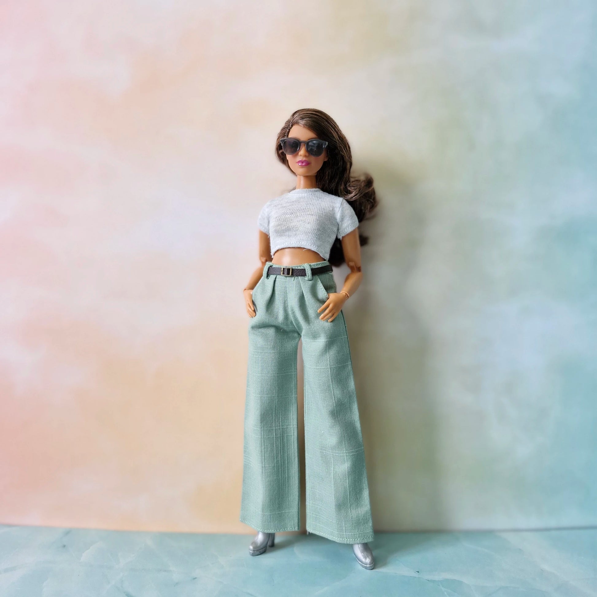 Barbie doll wearing a white crop top and light green pants against a gradient background