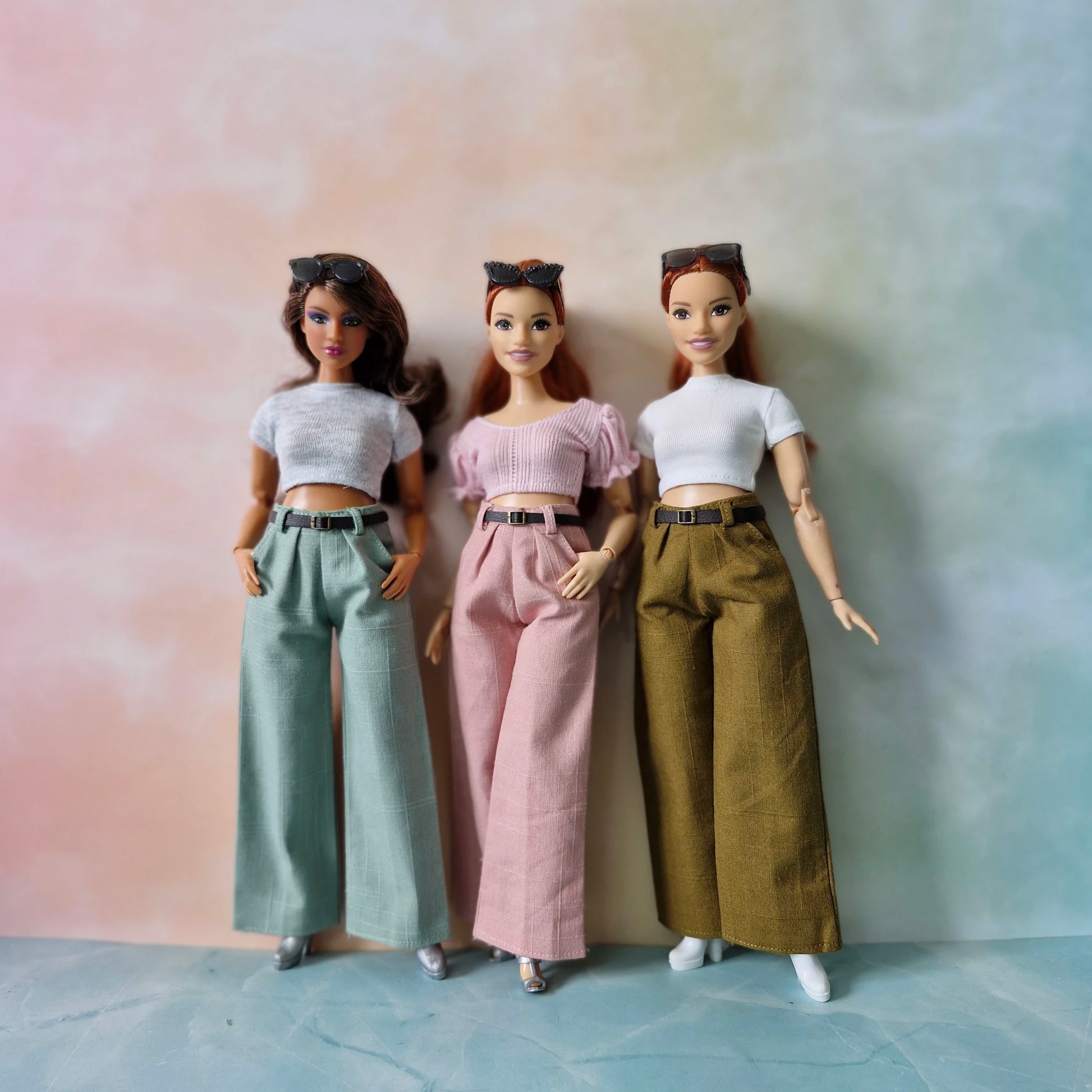 Three dolls wearing different outfits against a gradient background