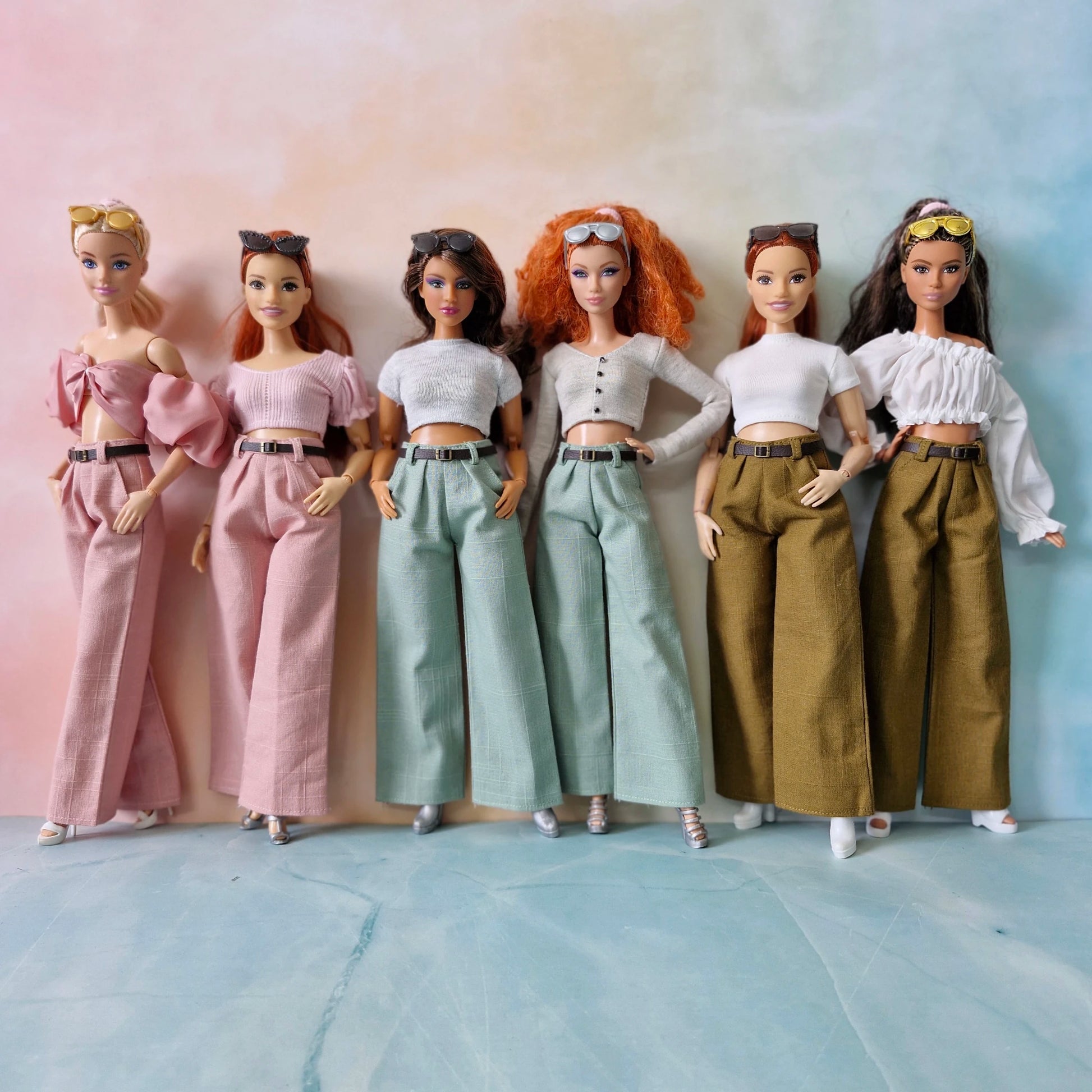 Six Barbie dolls in different outfits standing against a gradient background