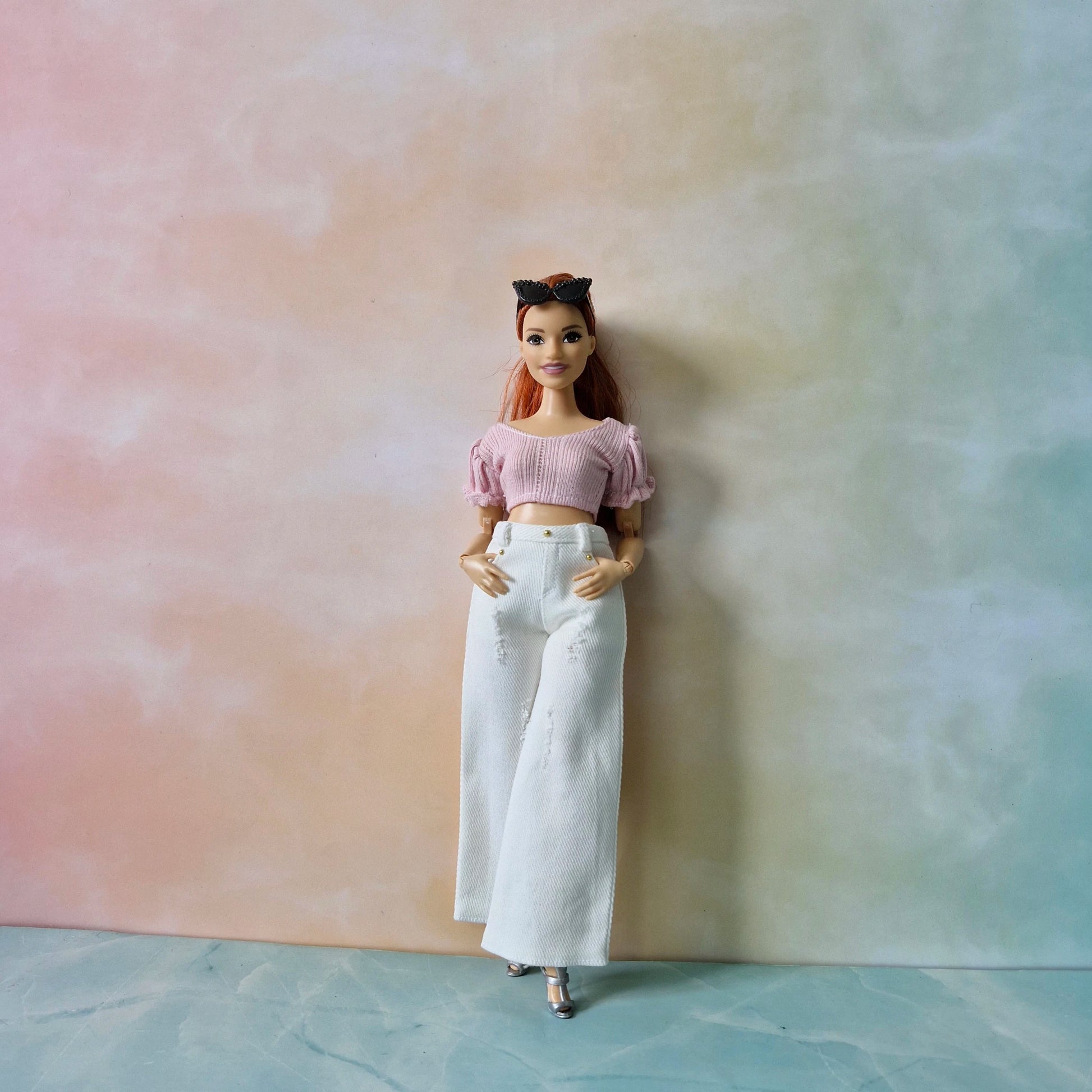 Barbie doll wearing a pink top and white pants against a gradient background