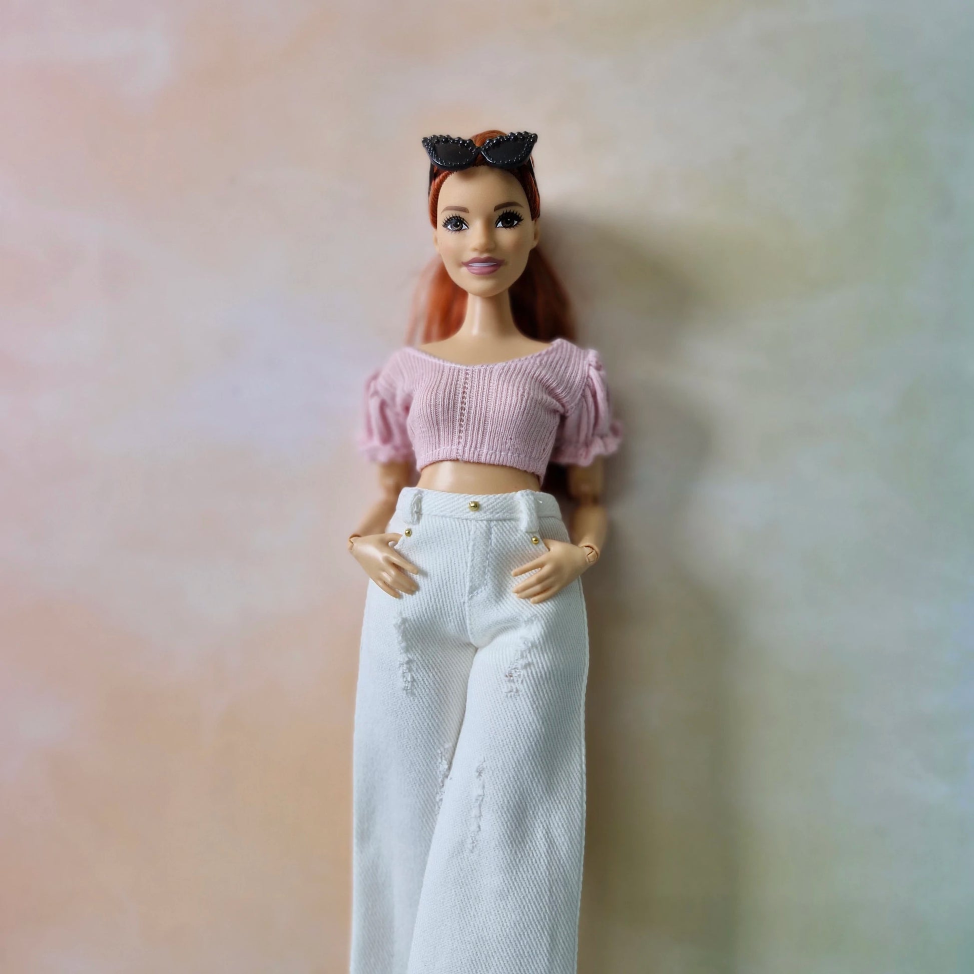 Barbie doll wearing a pink top and white pants against a soft, blurred background