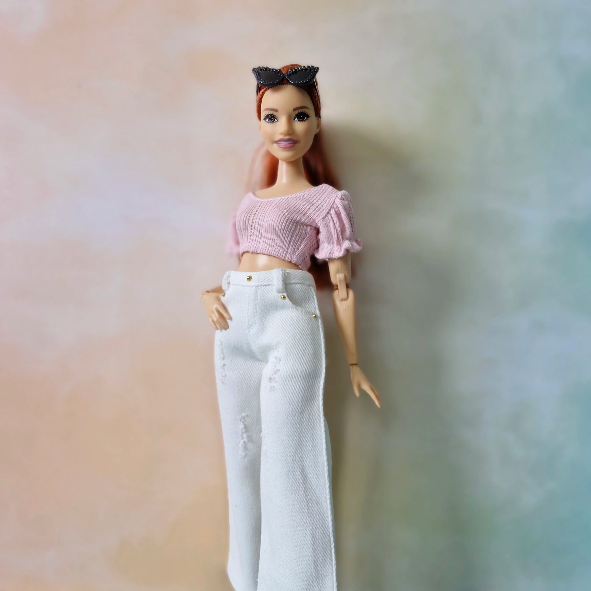 Barbie doll wearing a pink top and white pants against a blurred background