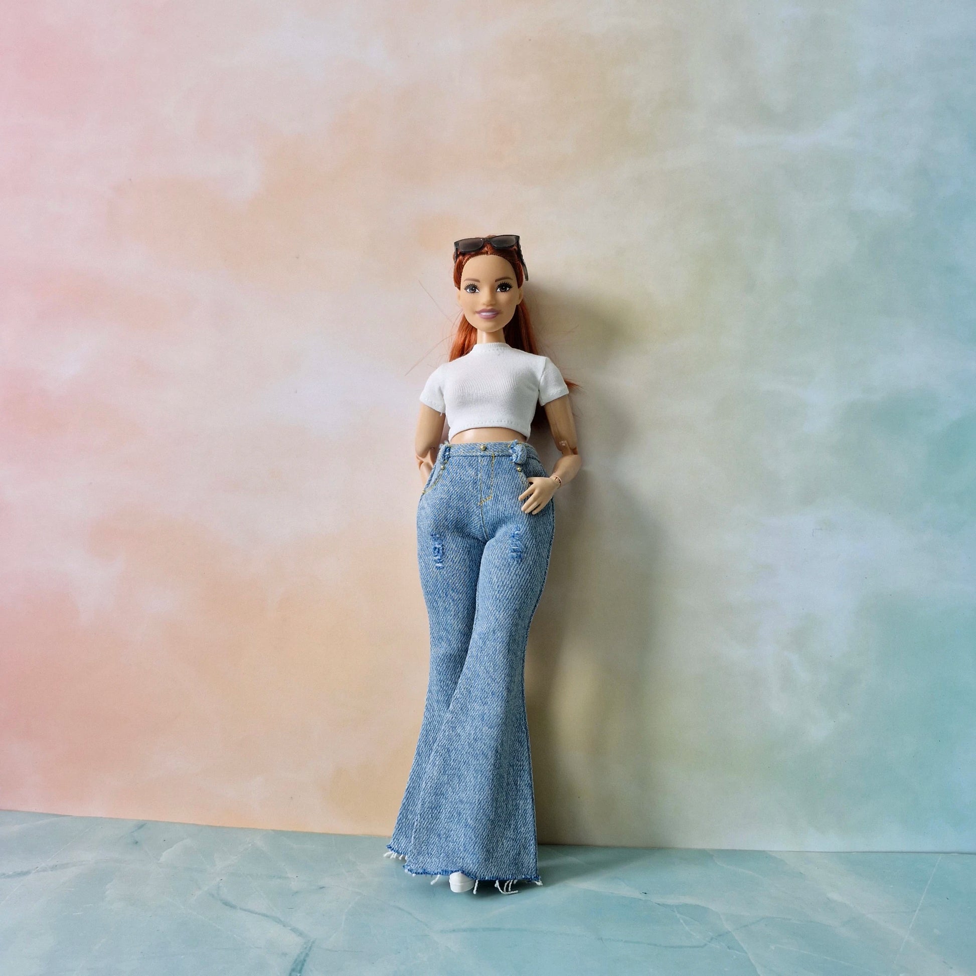 Barbie doll wearing a white top and blue jeans against a pastel gradient background
