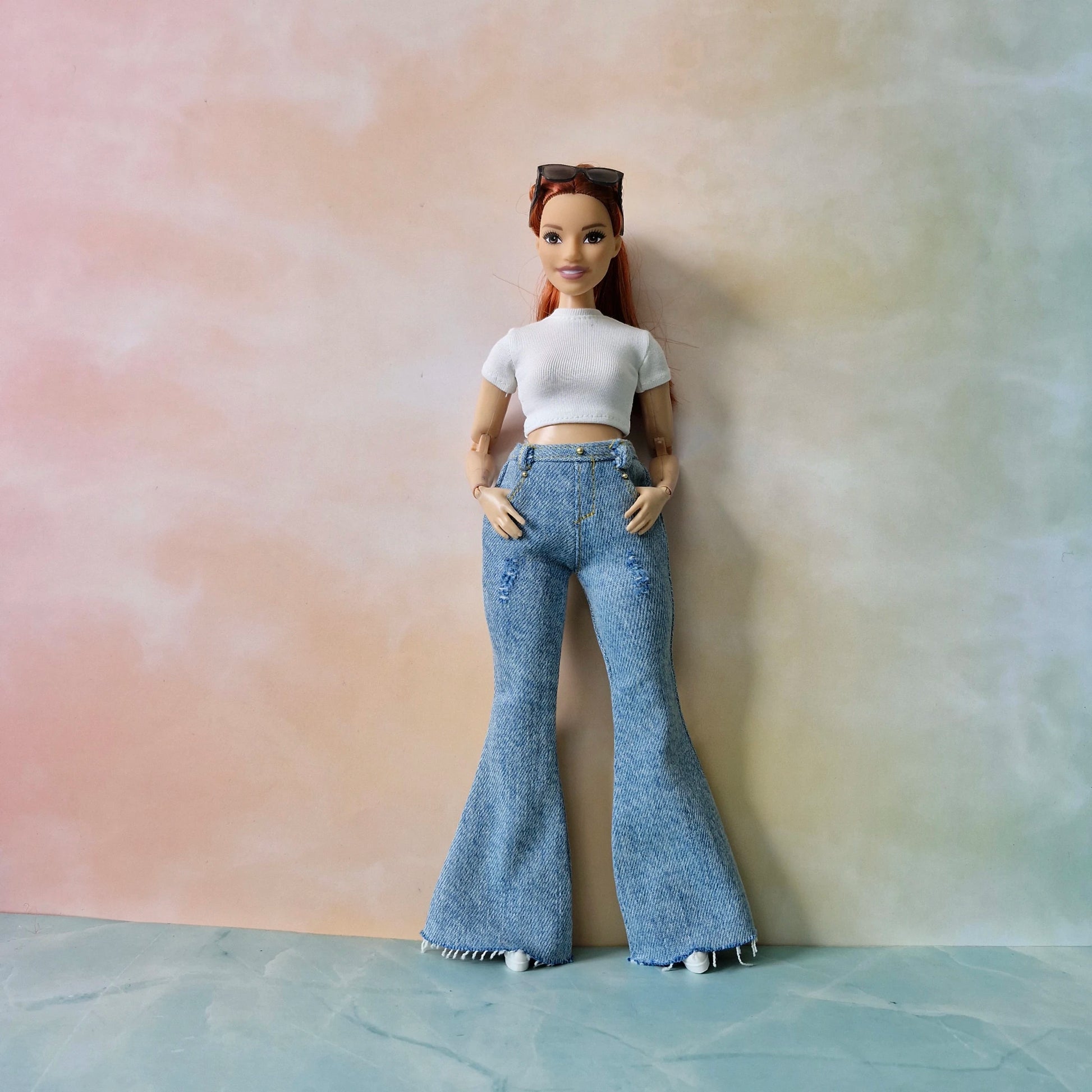 Barbie doll wearing a white crop top and blue flared jeans against a pastel gradient background