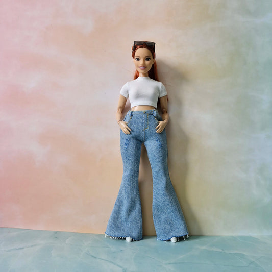 Barbie doll wearing a white crop top and blue flared jeans against a pastel gradient background