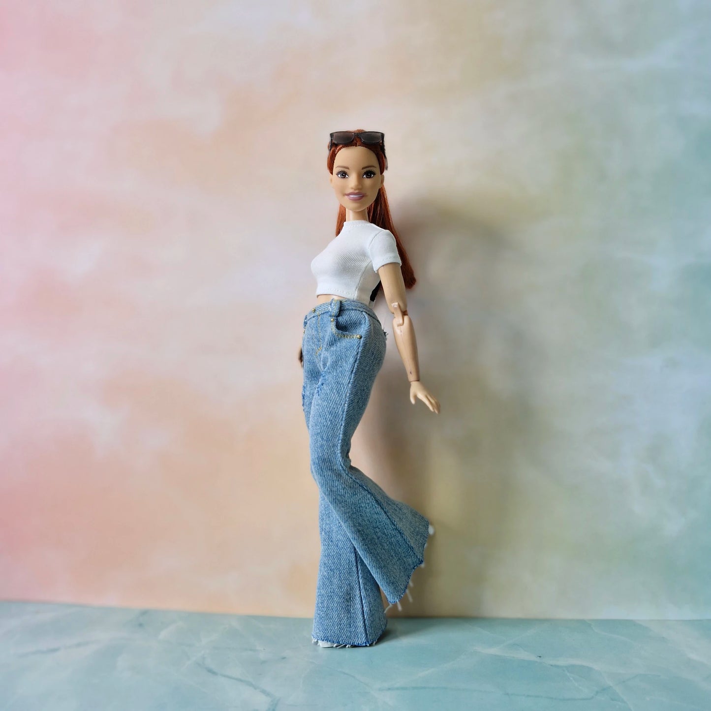Barbie doll wearing a white top and blue jeans against a gradient background