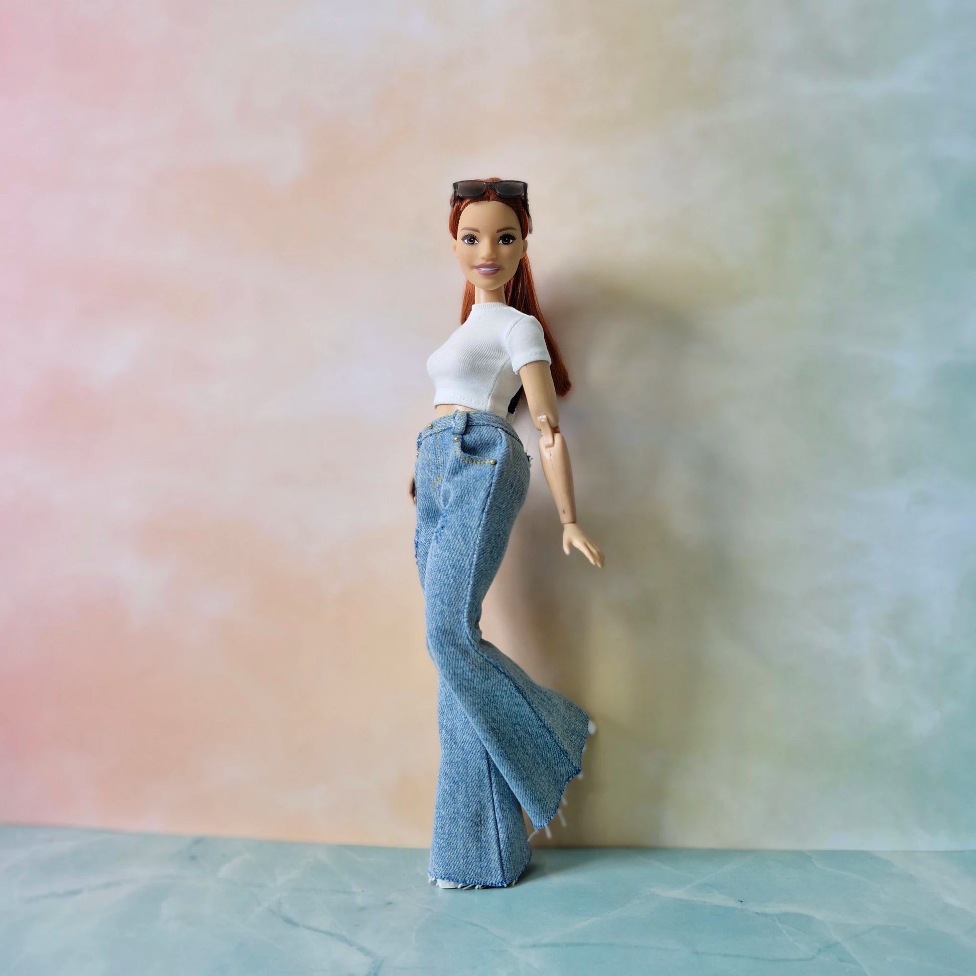 Barbie doll wearing a white top and blue jeans against a gradient background