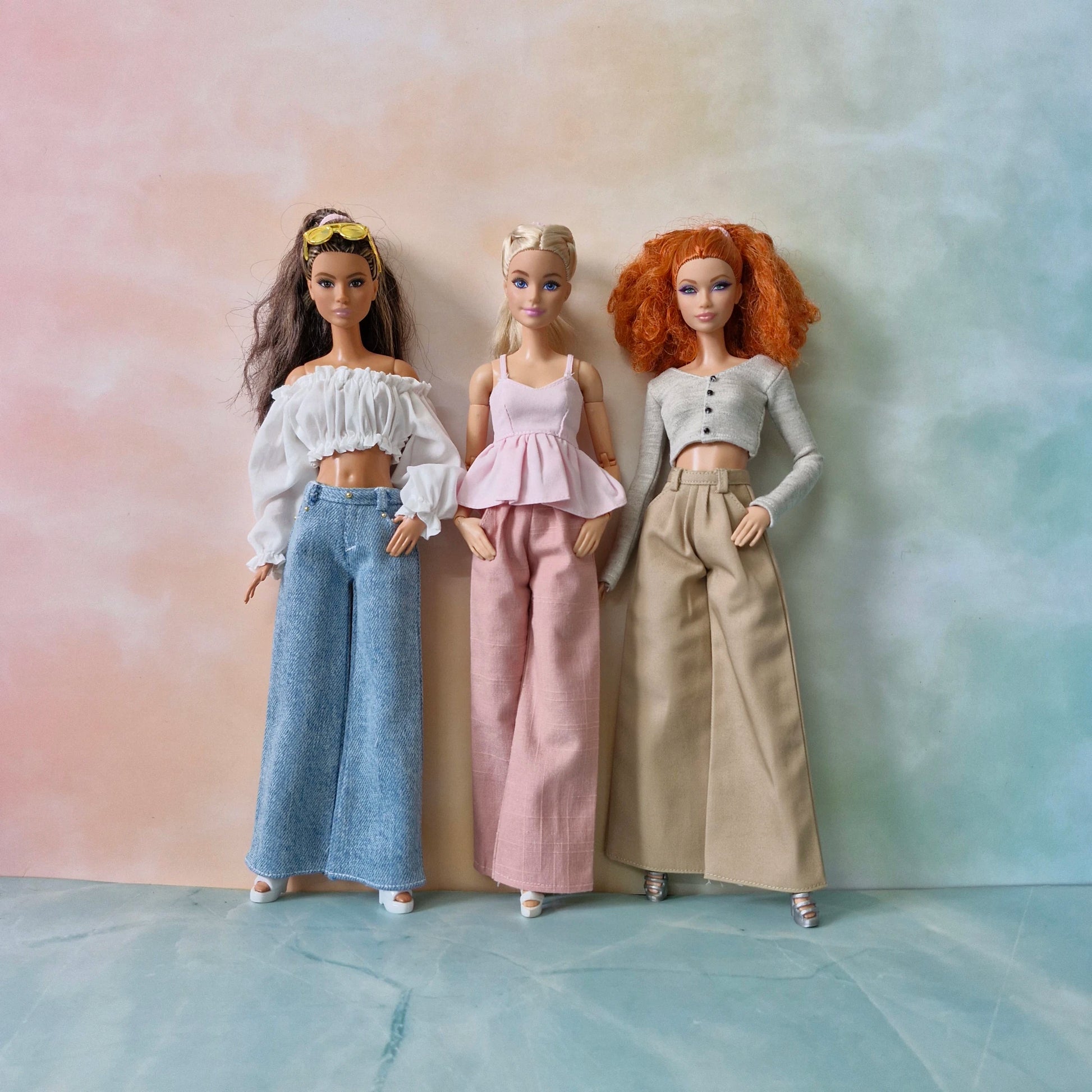 Three dolls with different hairstyles and outfits standing against a gradient background