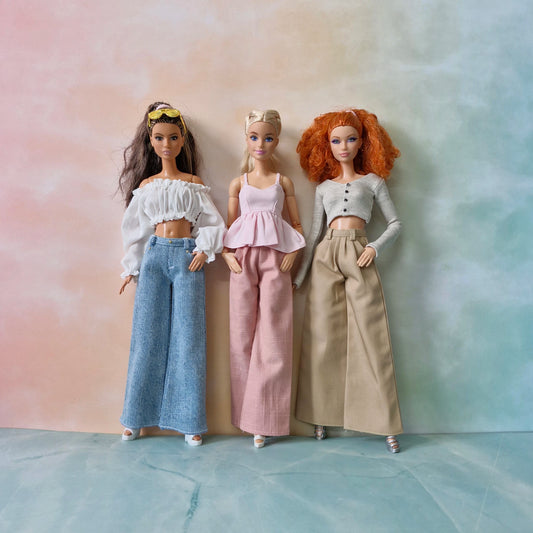 Three dolls with different hairstyles and outfits standing against a gradient background