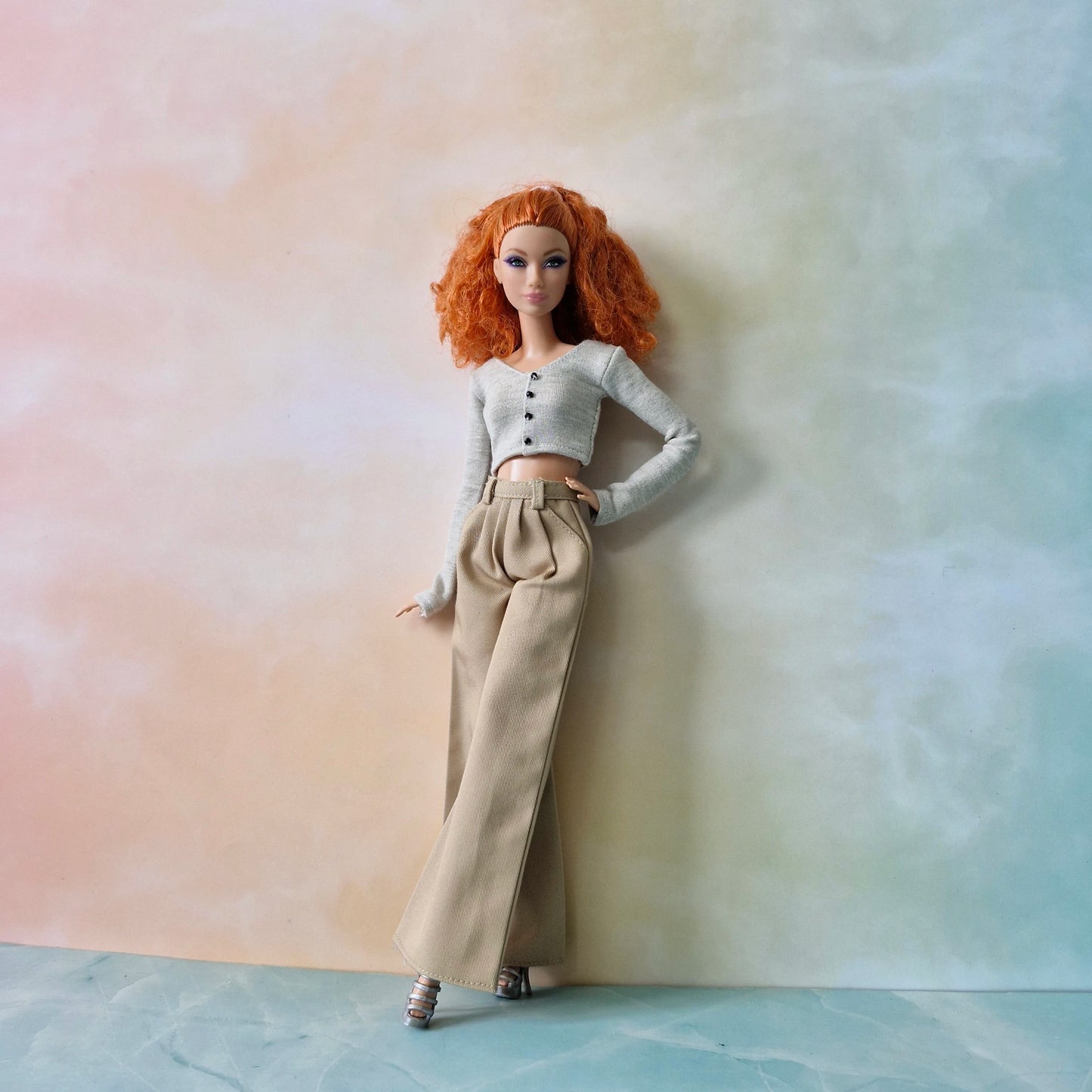 Barbie doll with red hair wearing a white top and beige pants against a pastel background