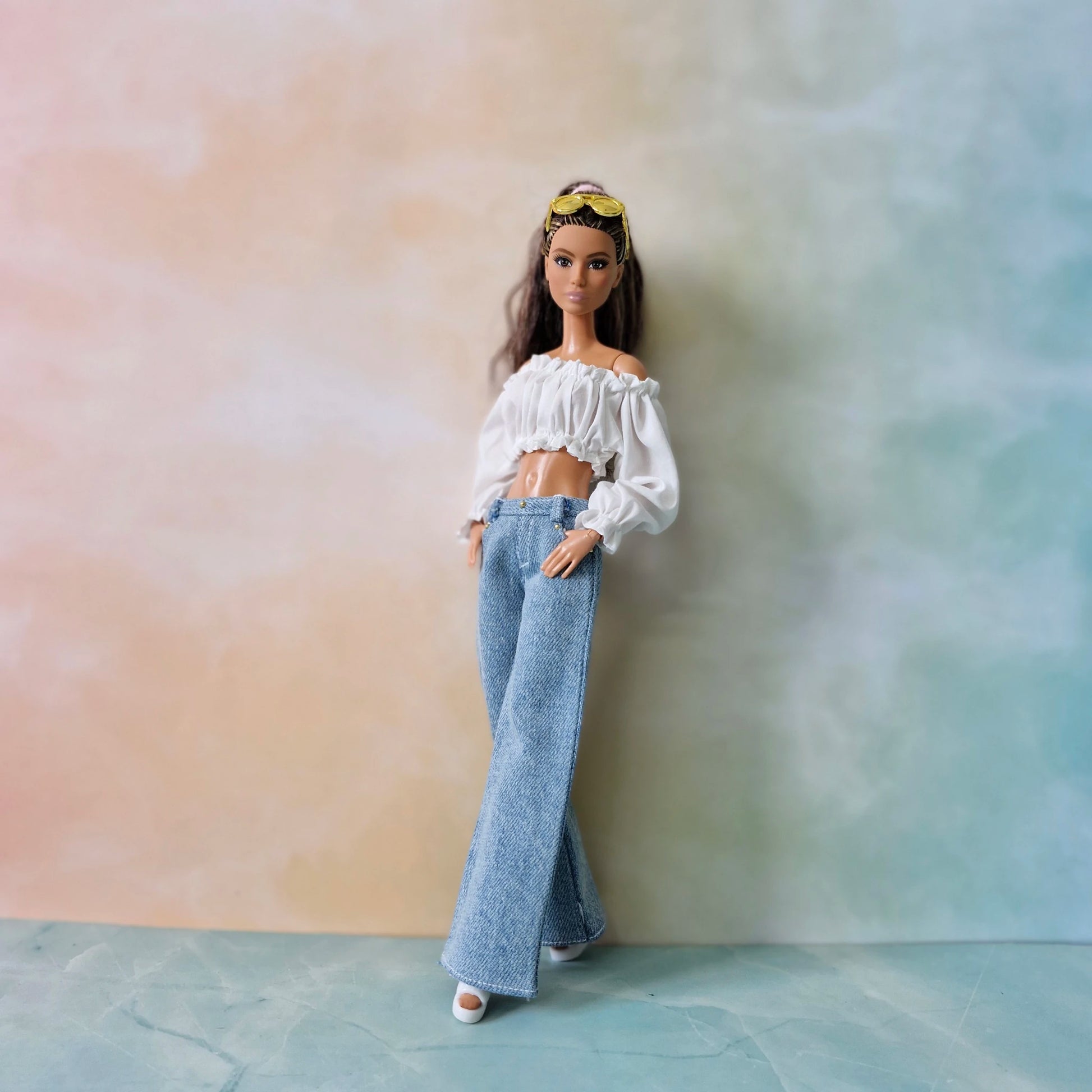 Barbie doll wearing a white top and blue jeans against a gradient wall.