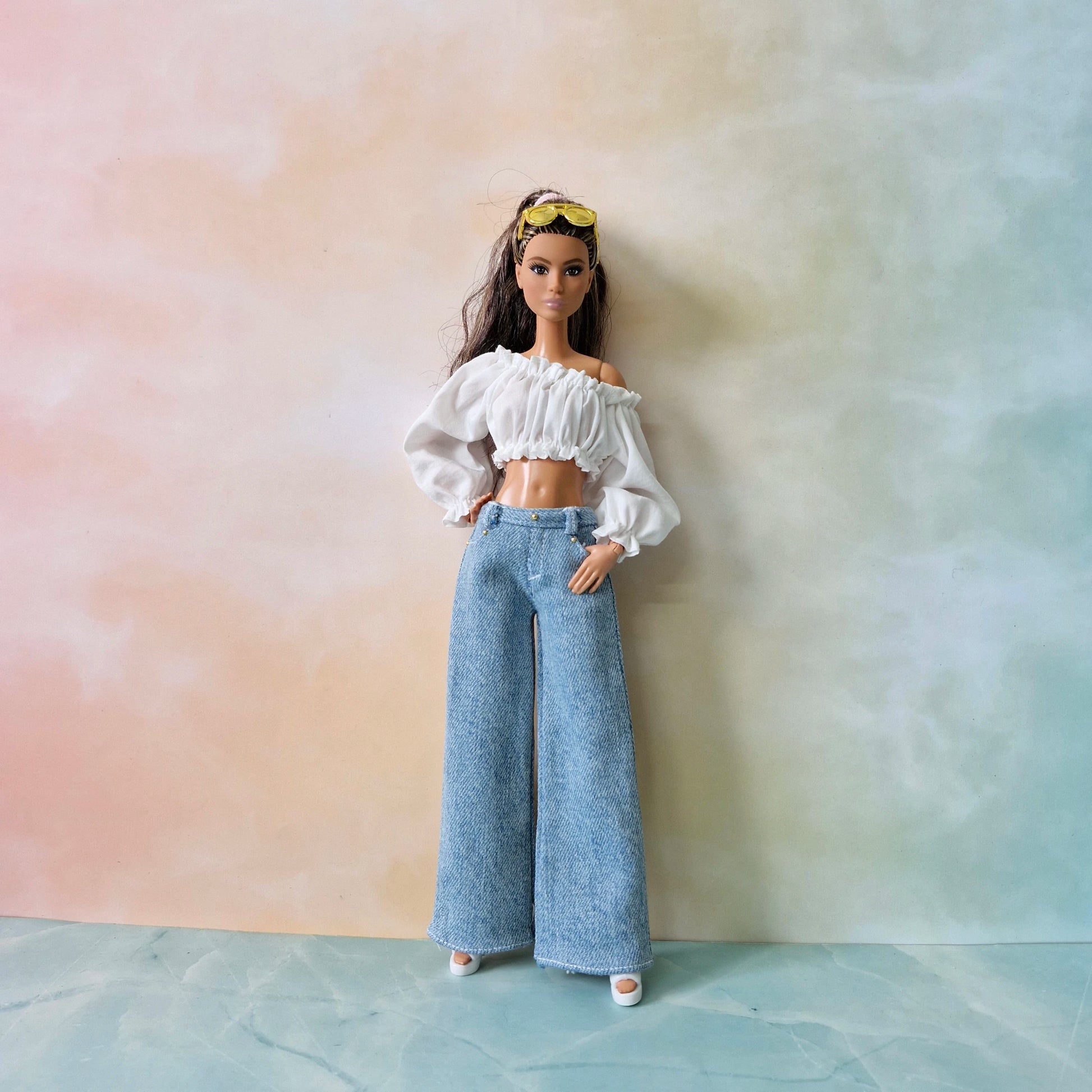 Barbie doll wearing a white top and blue pants against a pastel gradient background