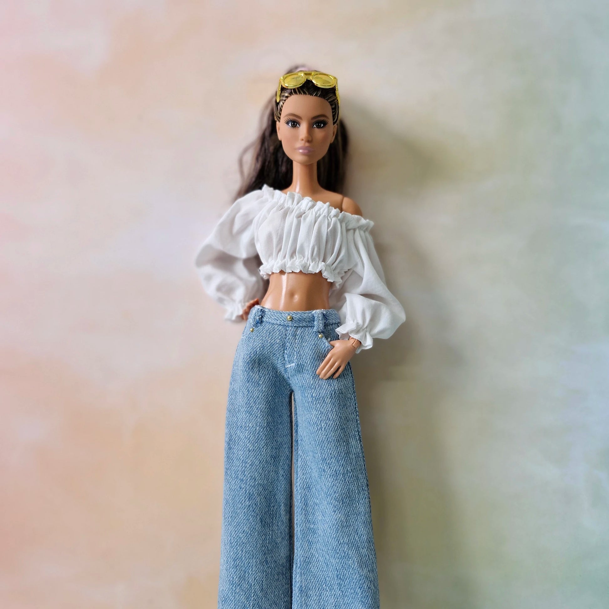 Barbie doll wearing a white top and blue jeans against a soft, multicolored background