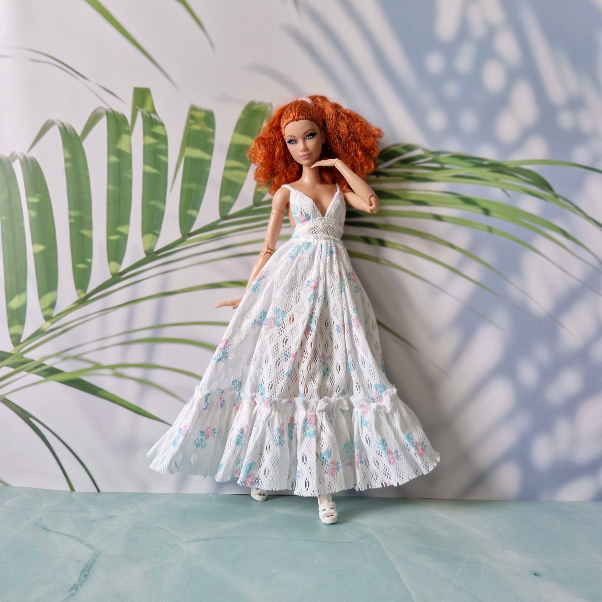 Doll in a white floral dress standing against a leafy green background