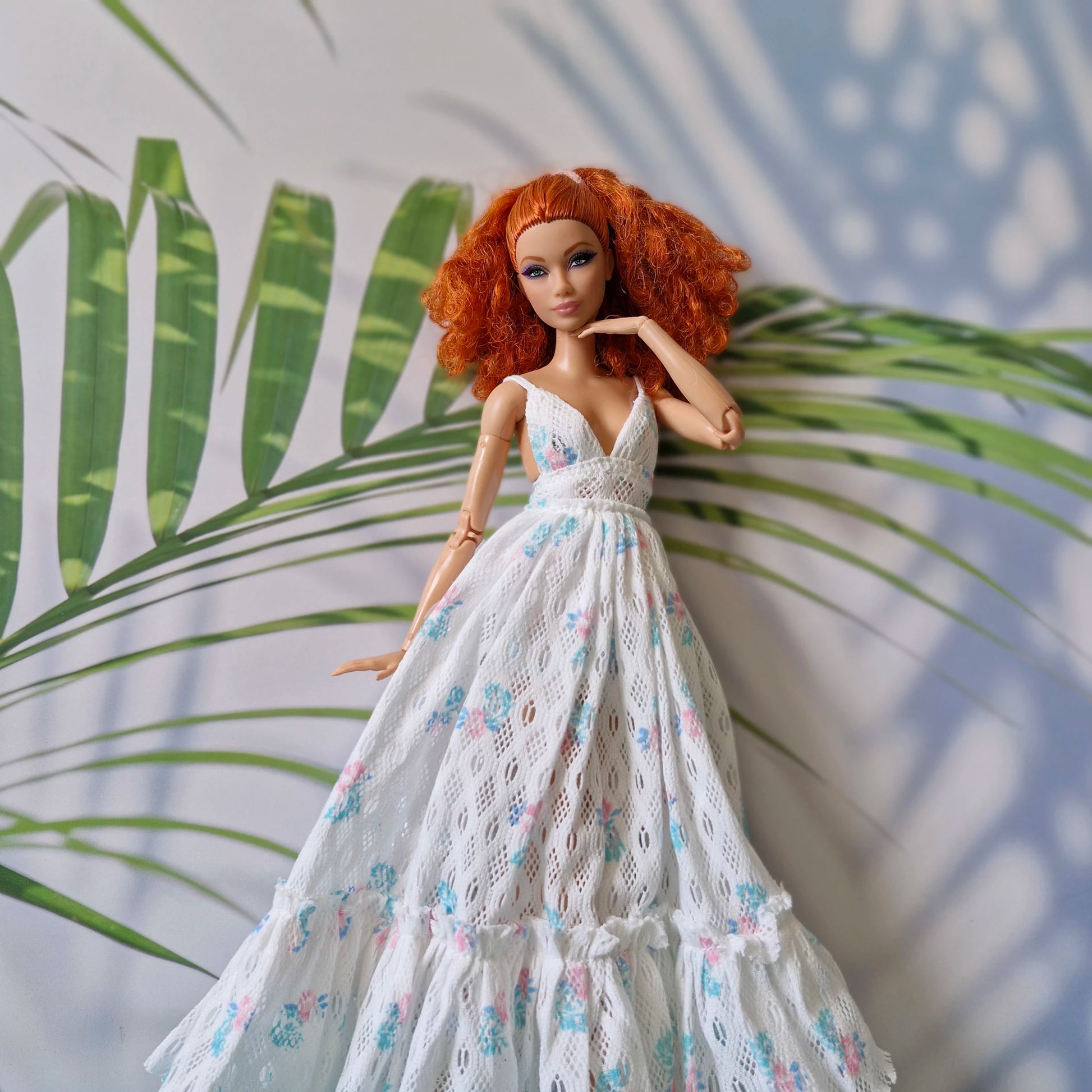 Barbie doll in a white floral dress standing against a leafy background