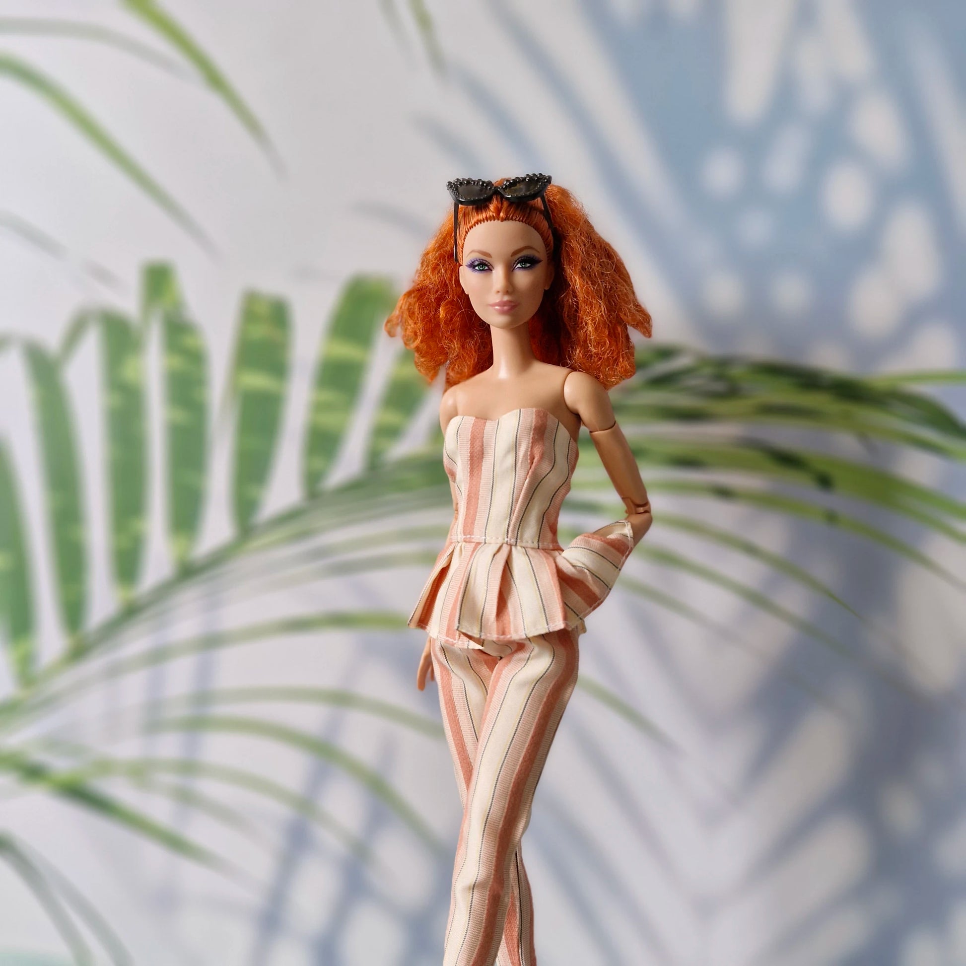 Barbie doll with red hair and a pink outfit standing against a leafy background