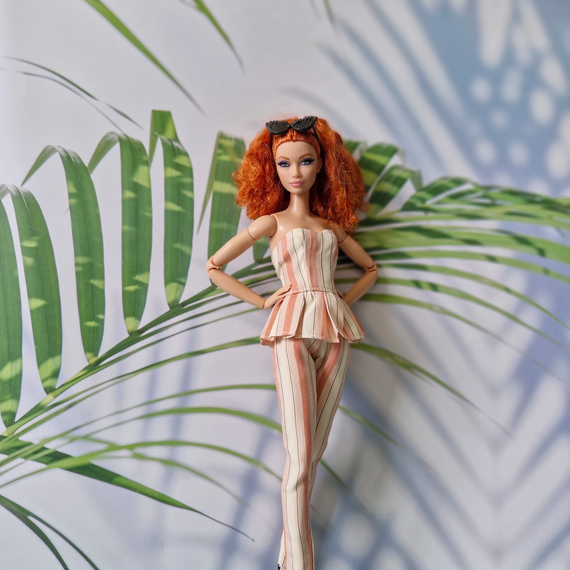 Barbie doll in a striped outfit standing against a leafy background