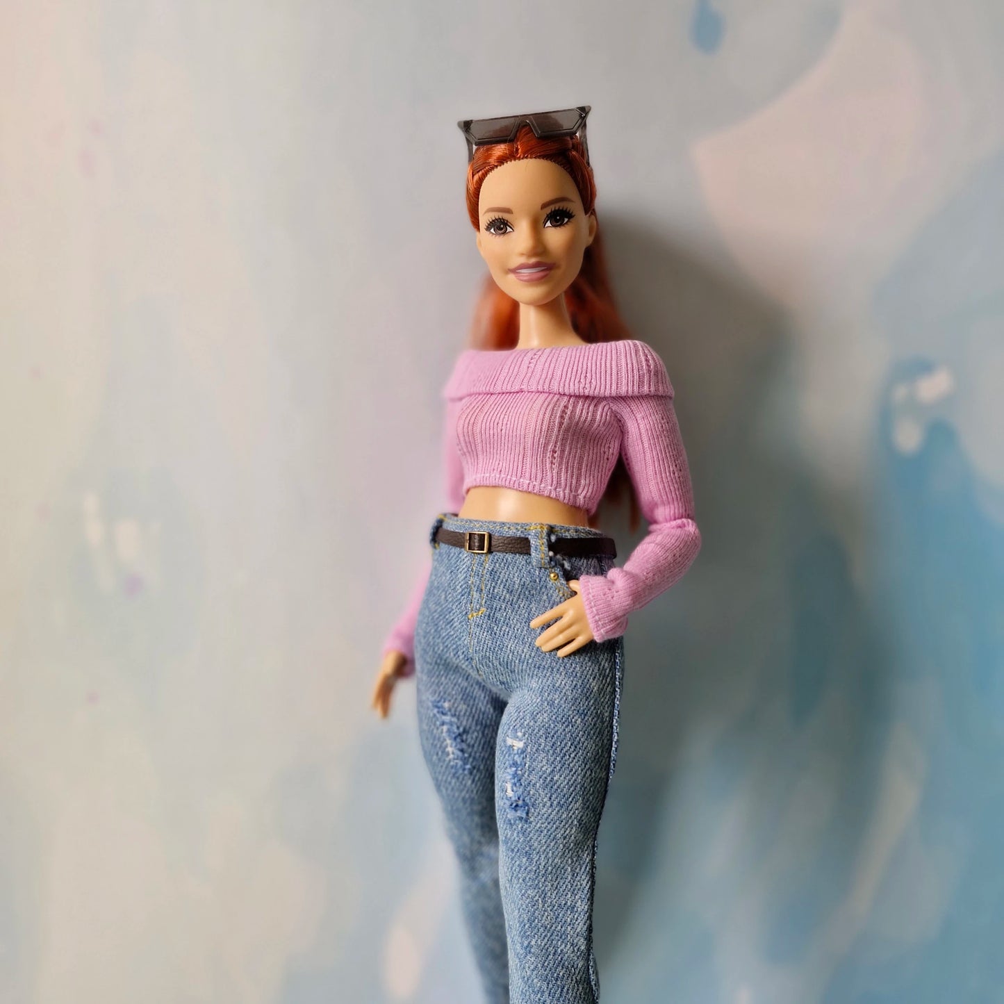 Barbie doll wearing a pink top and blue jeans against a neutral background