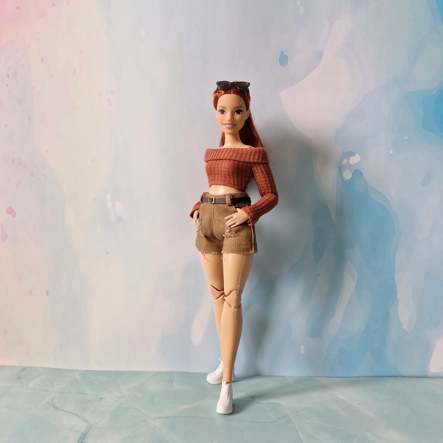 Barbie doll wearing a brown off-shoulder top and shorts against a pastel background