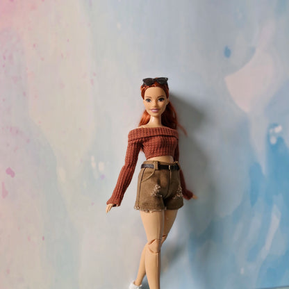 Barbie doll wearing a brown sweater and shorts against a textured light blue background