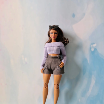 Barbie doll wearing a purple top and gray shorts against a light blue background