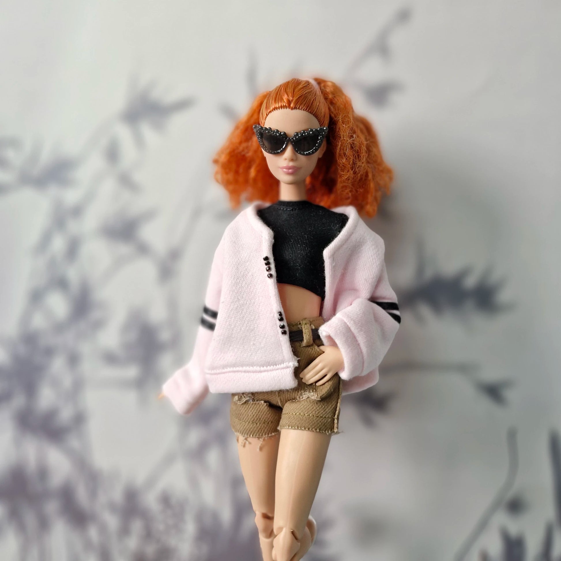 Barbie doll in pink cardigan with black crop top and khaki distressed shorts
