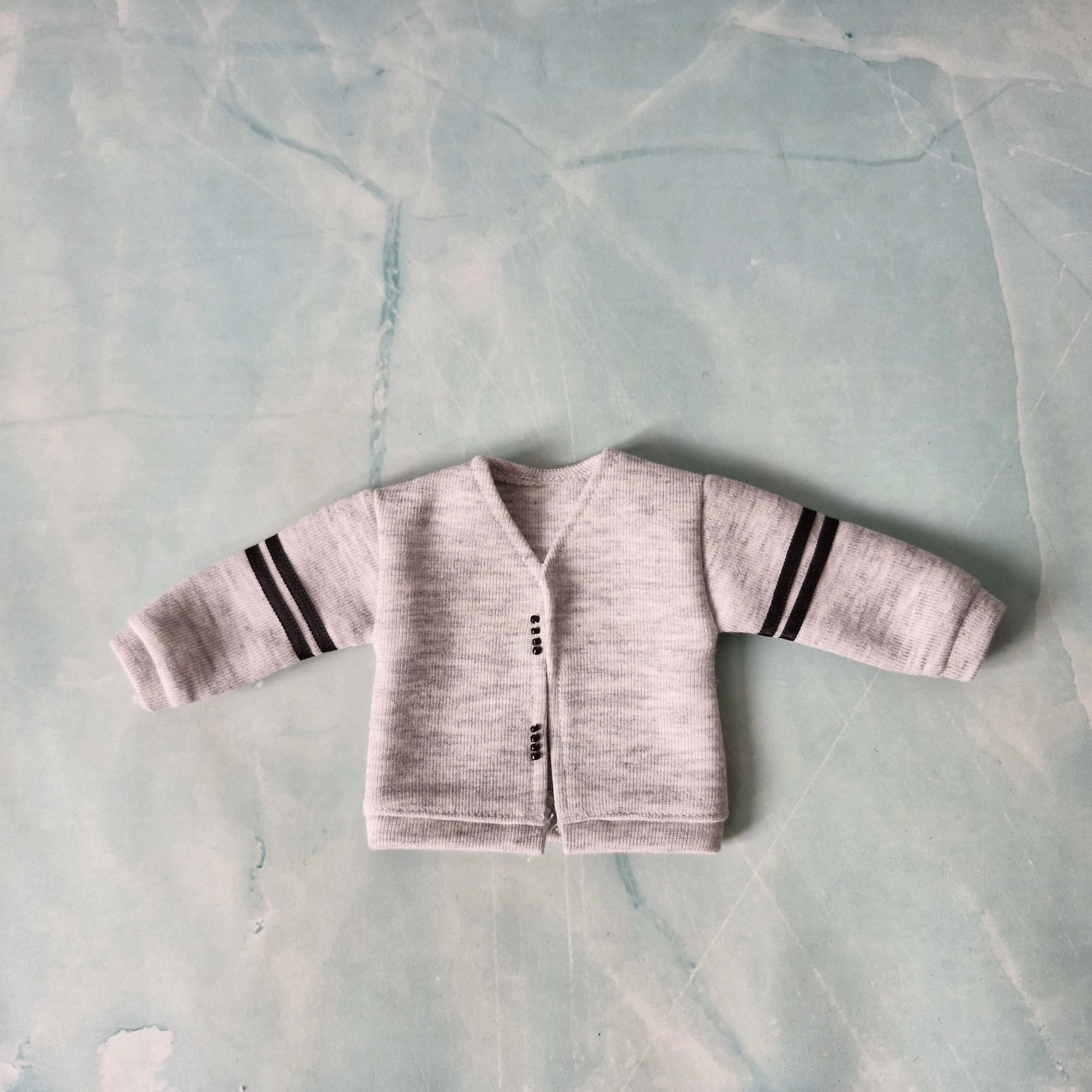 Baby cardigan with striped sleeves on a textured light blue background