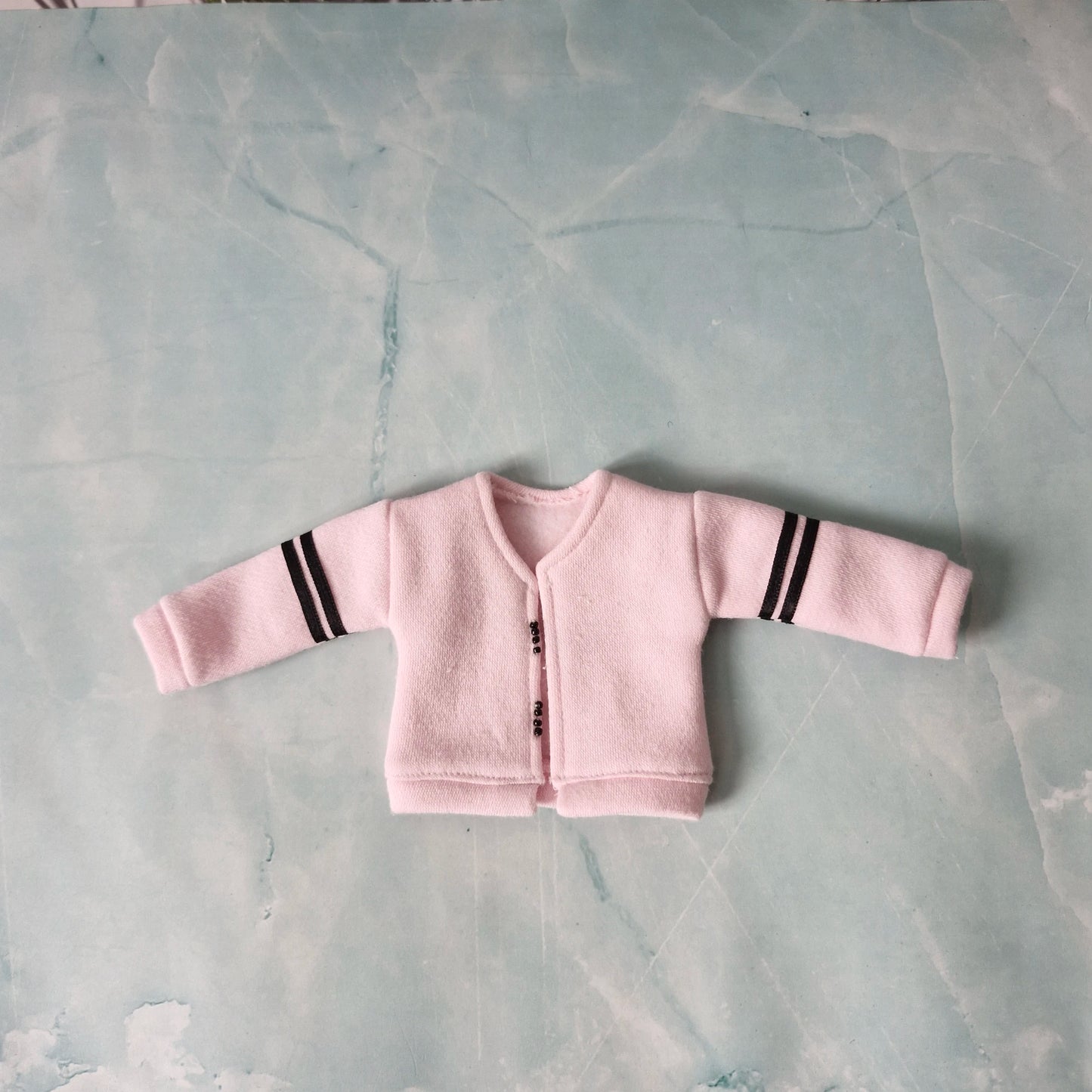 Pink baby cardigan with black stripes on a gray surface