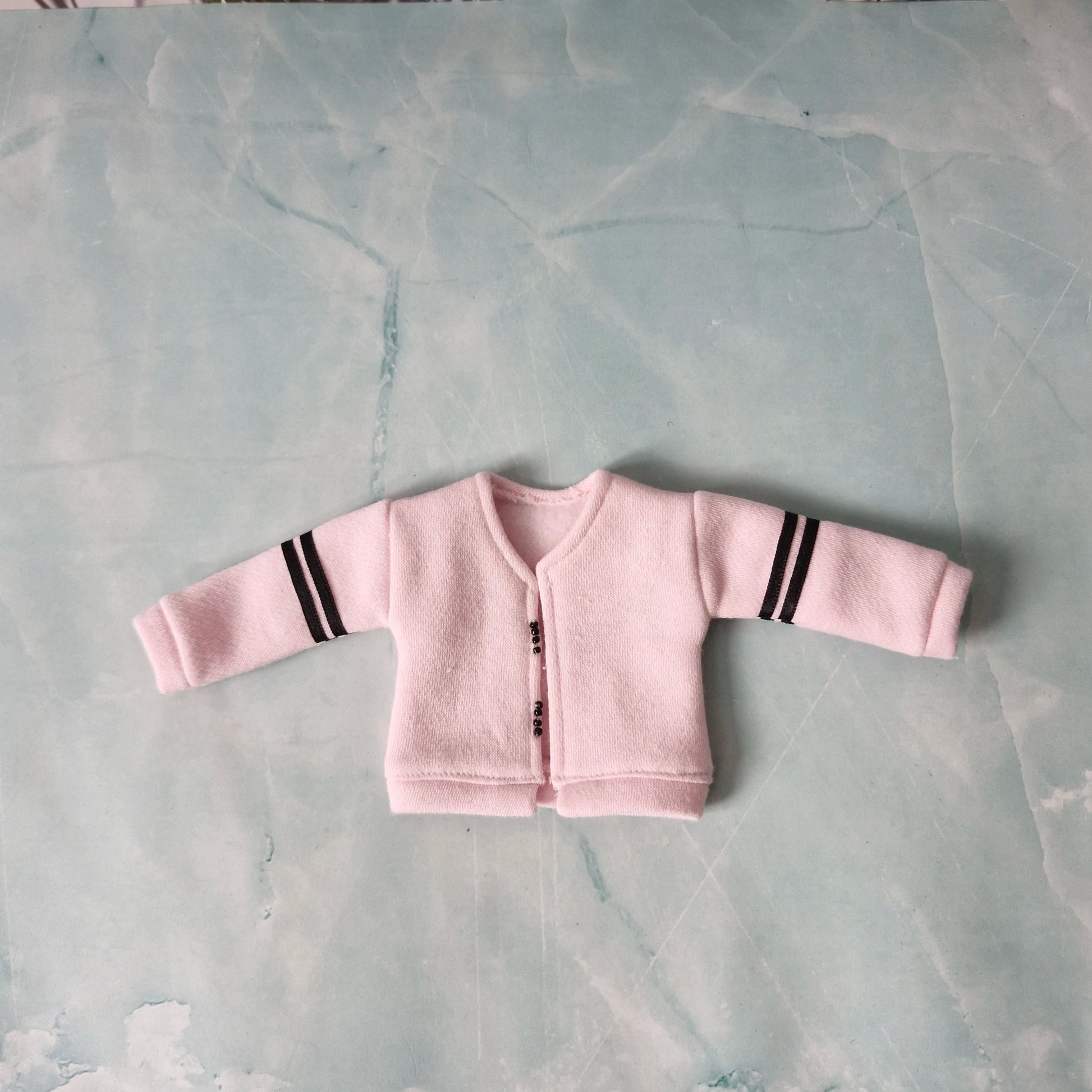 Pink baby cardigan with black stripes on a gray surface