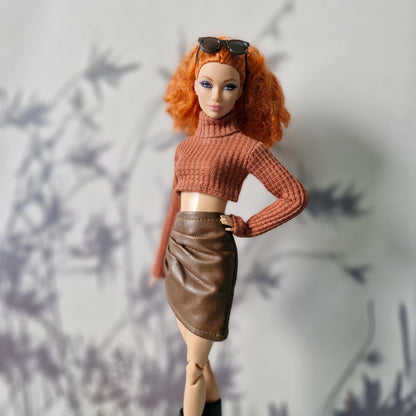 Barbie doll with red hair wearing a brown sweater and leather skirt against a neutral background