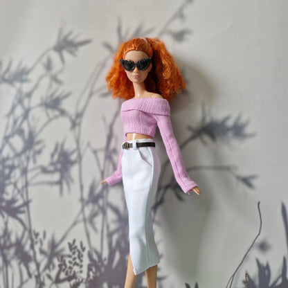 Barbie doll with red hair and sunglasses against a gray wall with plant shadows