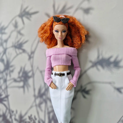 Barbie doll with red hair wearing a pink top and white pants against a neutral background